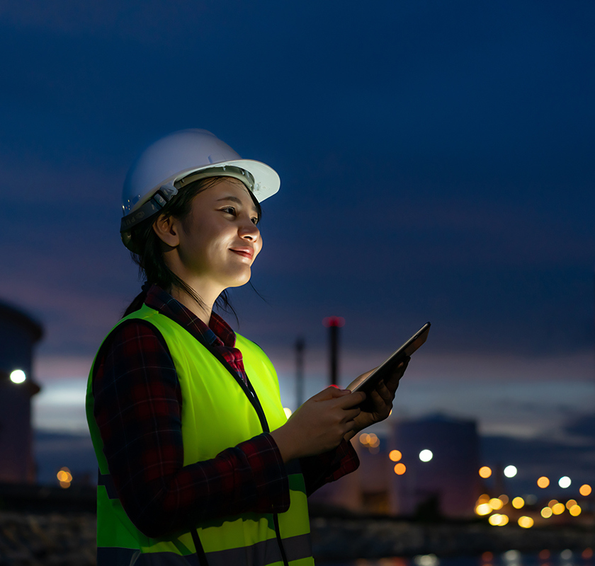 Asian woman petrochemical engineer working at night with digital tablet Inside oil and gas refinery plant industry factory at night for inspector safety quality control.